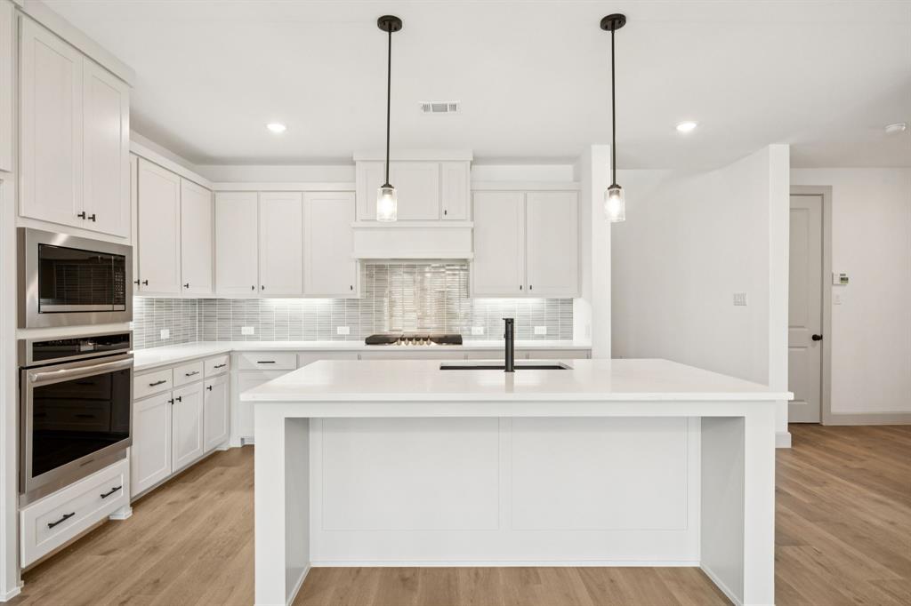 4180 Kestrel Street Prosper, TX 75078 - Photo 5 of 23 a kitchen with stainless steel appliances granite countertop a sink a stove a refrigerator and white cabinets with wooden floor