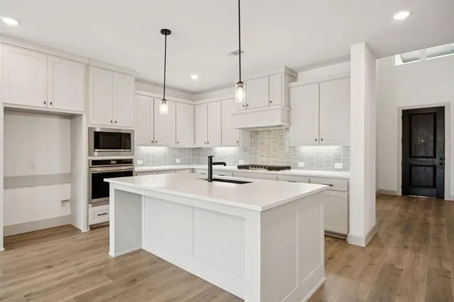 a open kitchen with granite countertop a stove a sink dishwasher a refrigerator and white cabinets with wooden floor