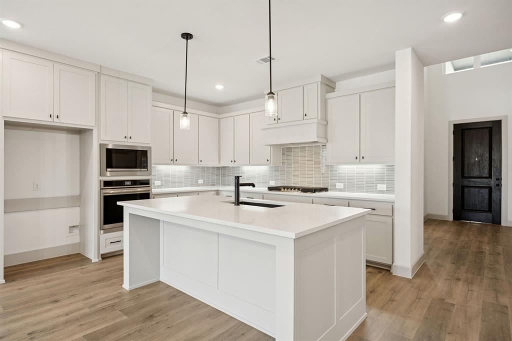 4180 Kestrel Street Prosper, TX 75078 - Photo 7 of 23 a kitchen with stainless steel appliances granite countertop a sink stove a refrigerator and white cabinets with wooden floor