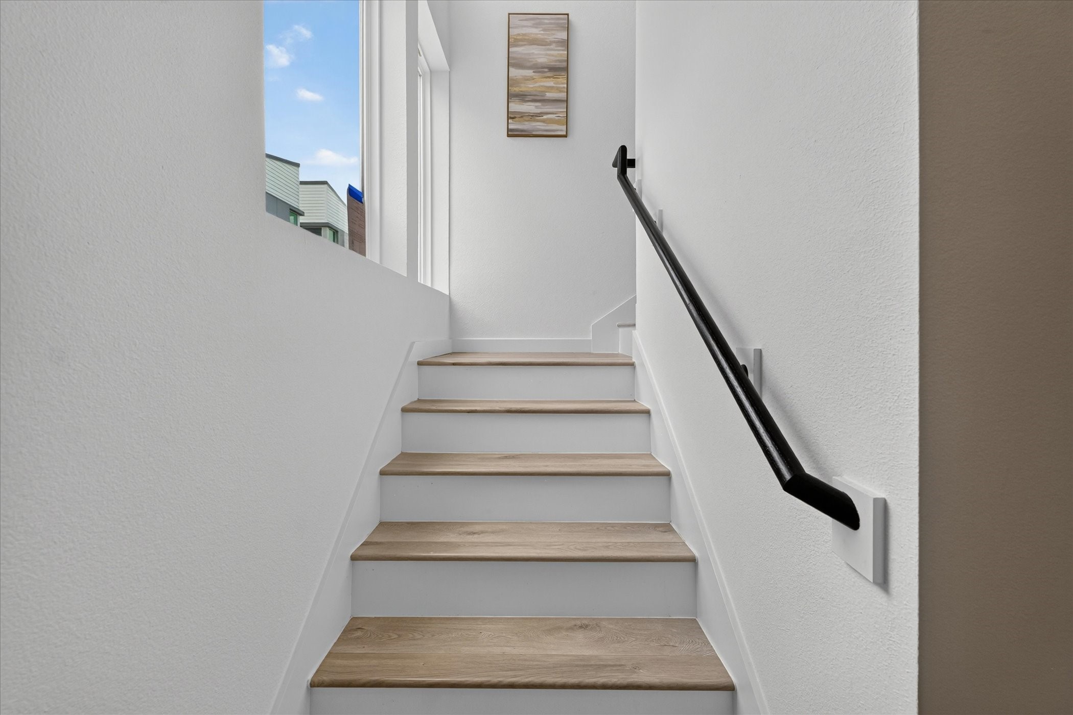 2000 Riverside Farms Road, Unit 8101 Austin, TX 78741 - Photo 12 of 41 This photo shows a modern staircase with light wood steps and a sleek black handrail, leading up to a bright landing with a window.