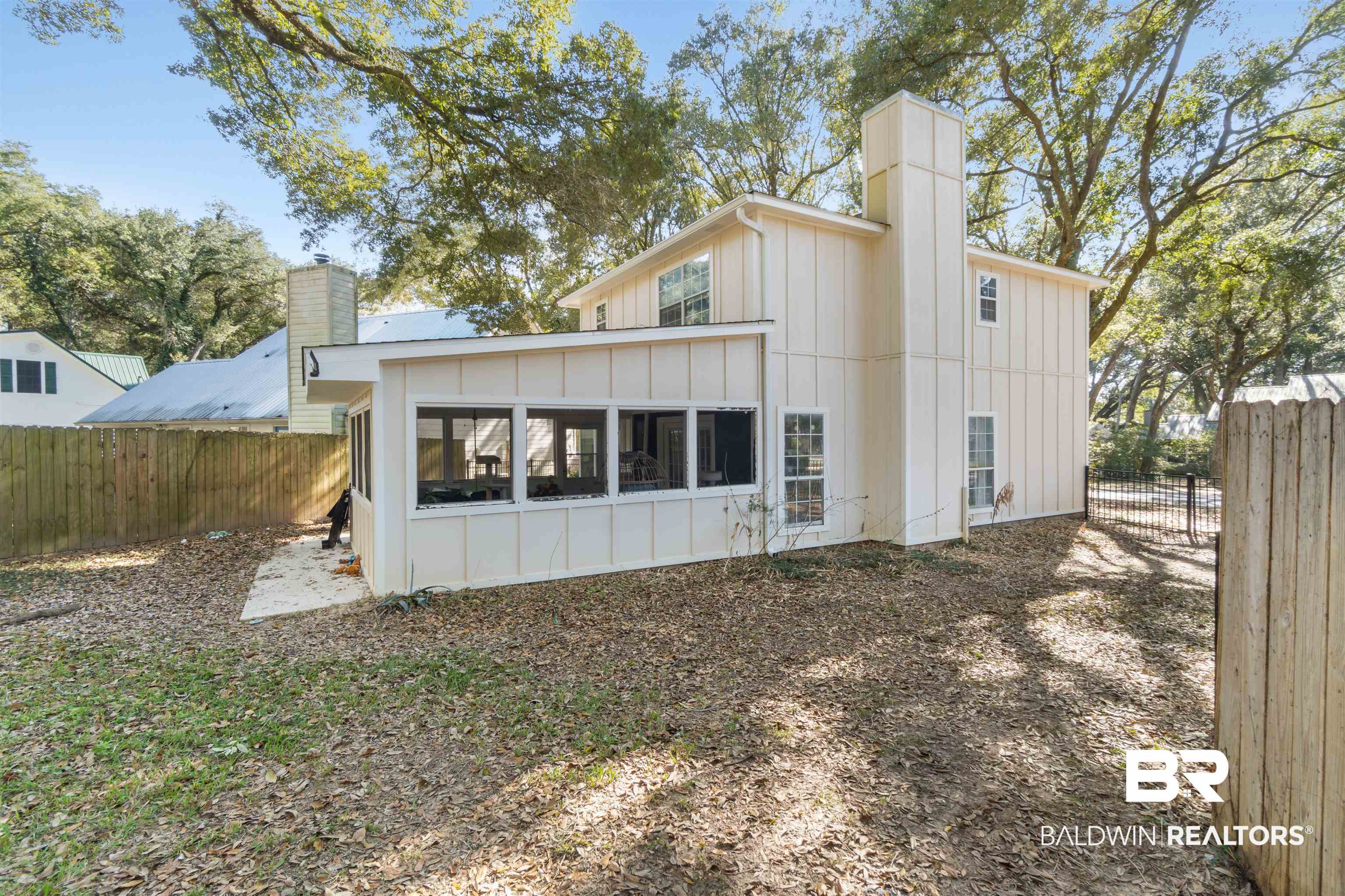Back of house featuring board and batten siding, a chimney, a fenced backyard, and a sunroom