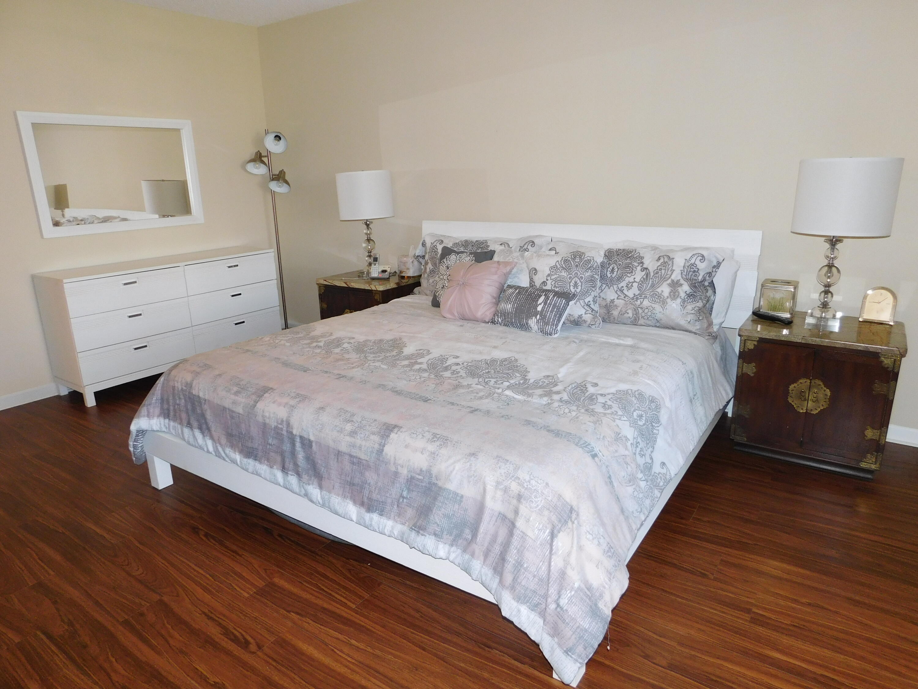 5235 Europa Drive, Unit E Boynton Beach, FL 33437 - Photo 15 of 57 a large bed sitting in a bedroom next to a lamp and a wooden floor