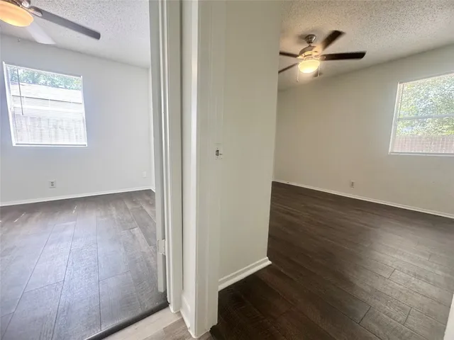 an empty room with wooden floor chandelier fan and windows