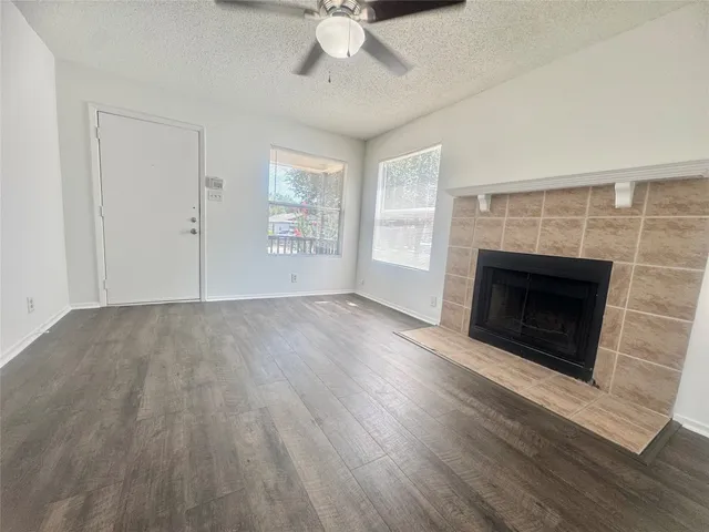 an empty room with wooden floor a fireplace a ceiling fan and windows