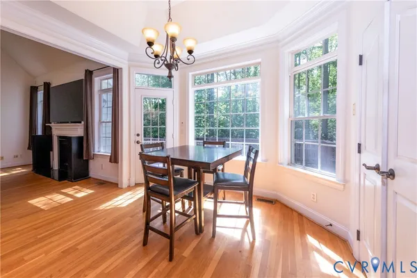 a dining room with wooden floor a chandelier a glass table and chairs