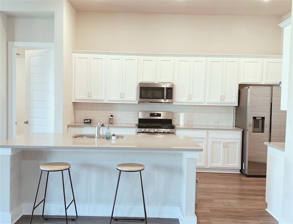 1304 Caprock Drive Forney, TX 75126 - Photo 10 of 15 Kitchen featuring white cabinetry, stainless steel appliances, a breakfast bar area, backsplash, and light wood finished floors