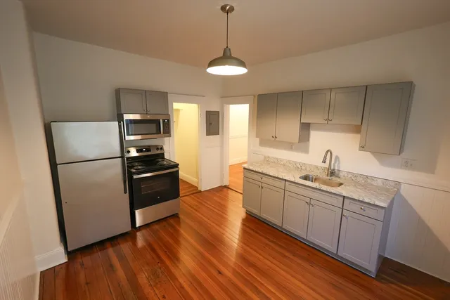 a kitchen with stainless steel appliances granite countertop a refrigerator a sink dishwasher a stove and white countertops with wooden floor