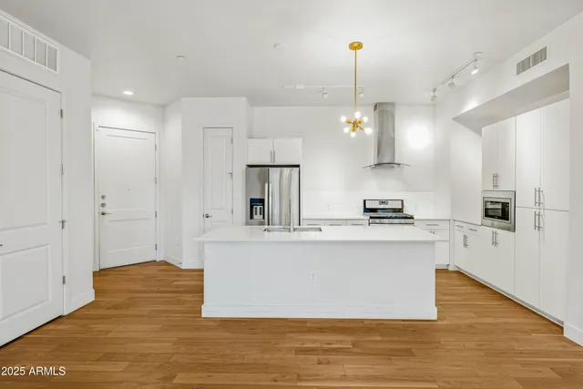 a large white kitchen with kitchen island a stove a sink a refrigerator and white cabinets with wooden floor