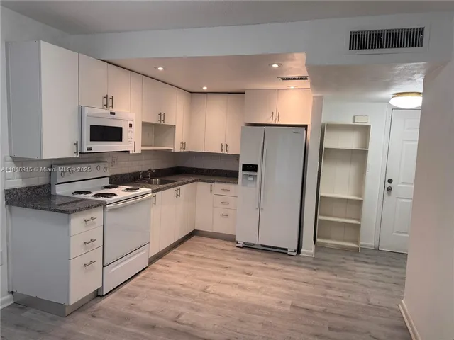 a kitchen with stainless steel appliances a stove top oven a sink a refrigerator white cabinets and wooden floor