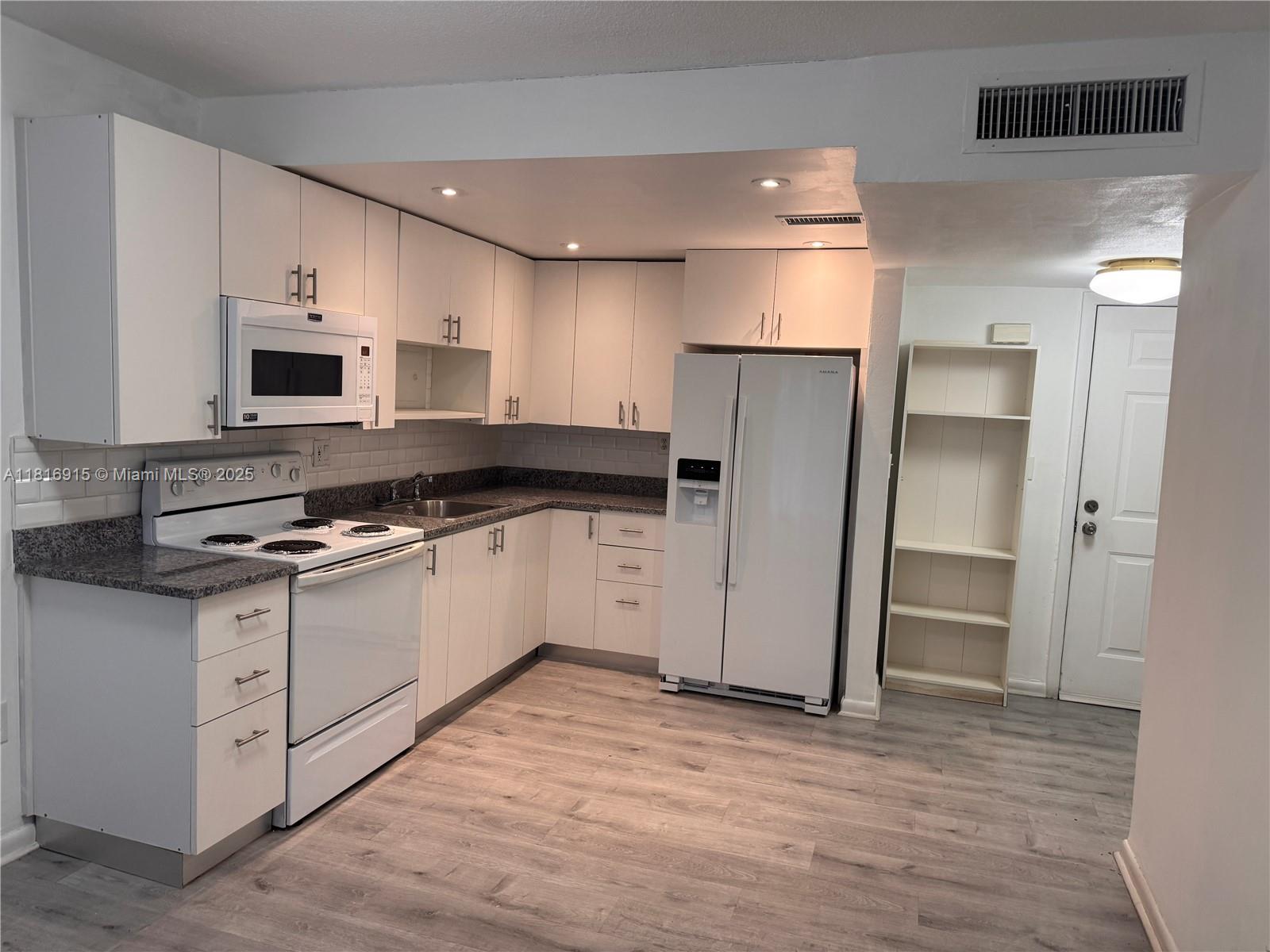 a kitchen with stainless steel appliances a stove top oven a sink a refrigerator white cabinets and wooden floor