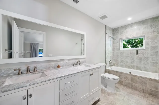 a bathroom with a granite countertop sink double mirror bathtub and toilet