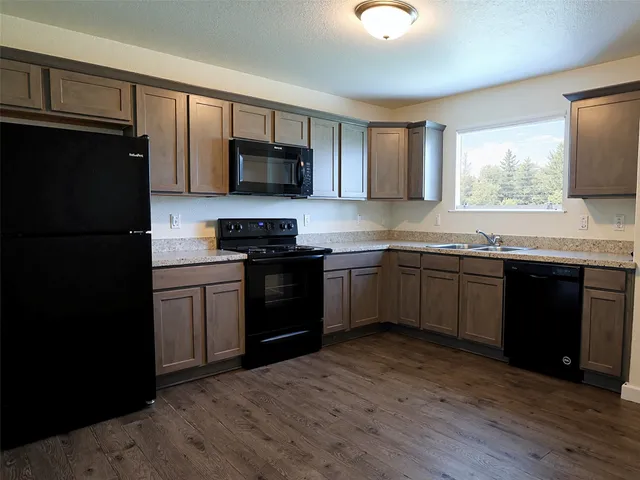 a kitchen with stainless steel appliances granite countertop a sink a stove top oven a refrigerator with wooden floors and cabinets