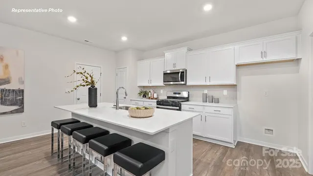 a kitchen with a sink a stove a refrigerator and white cabinets with wooden floor