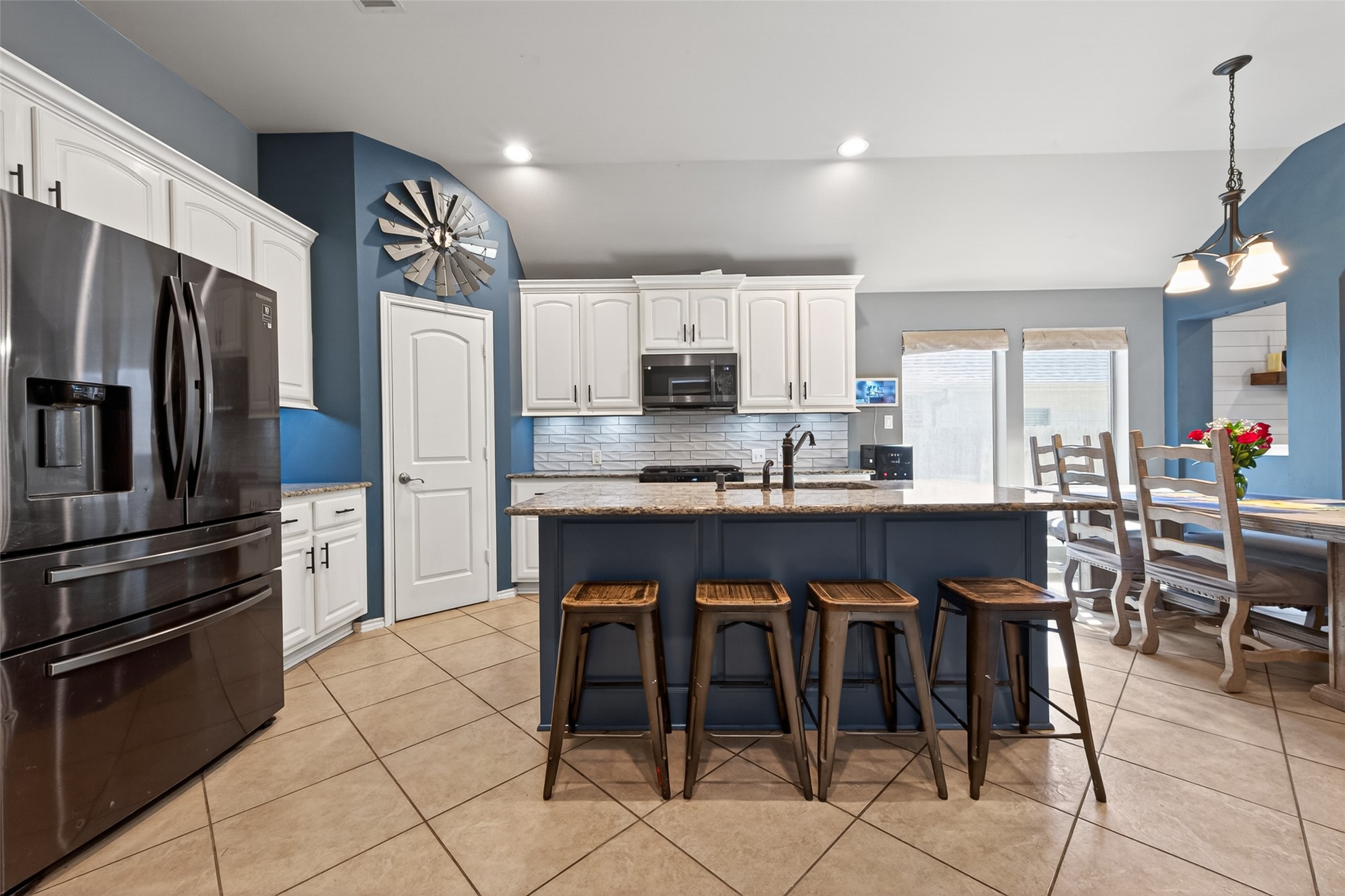 27443 Rebecca Field Lane Spring, TX 77386 - Photo 8 of 31 This kitchen features a modern design with white cabinetry, and a central island with seating for four. The space is accented by blue walls and a cozy dining area with ample natural light. Perfect for both cooking and entertaining.