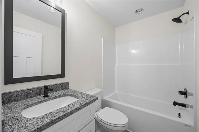 a bathroom with a granite countertop sink a toilet and shower