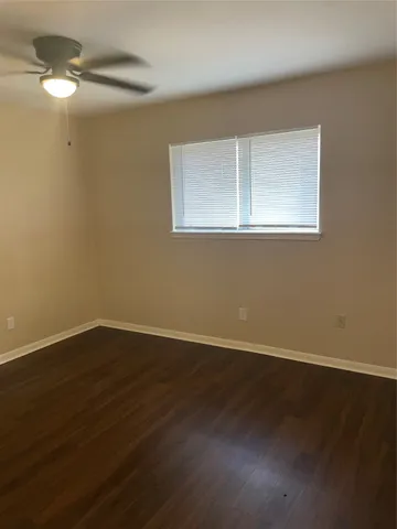 a view of an empty room with wooden floor fan and a window