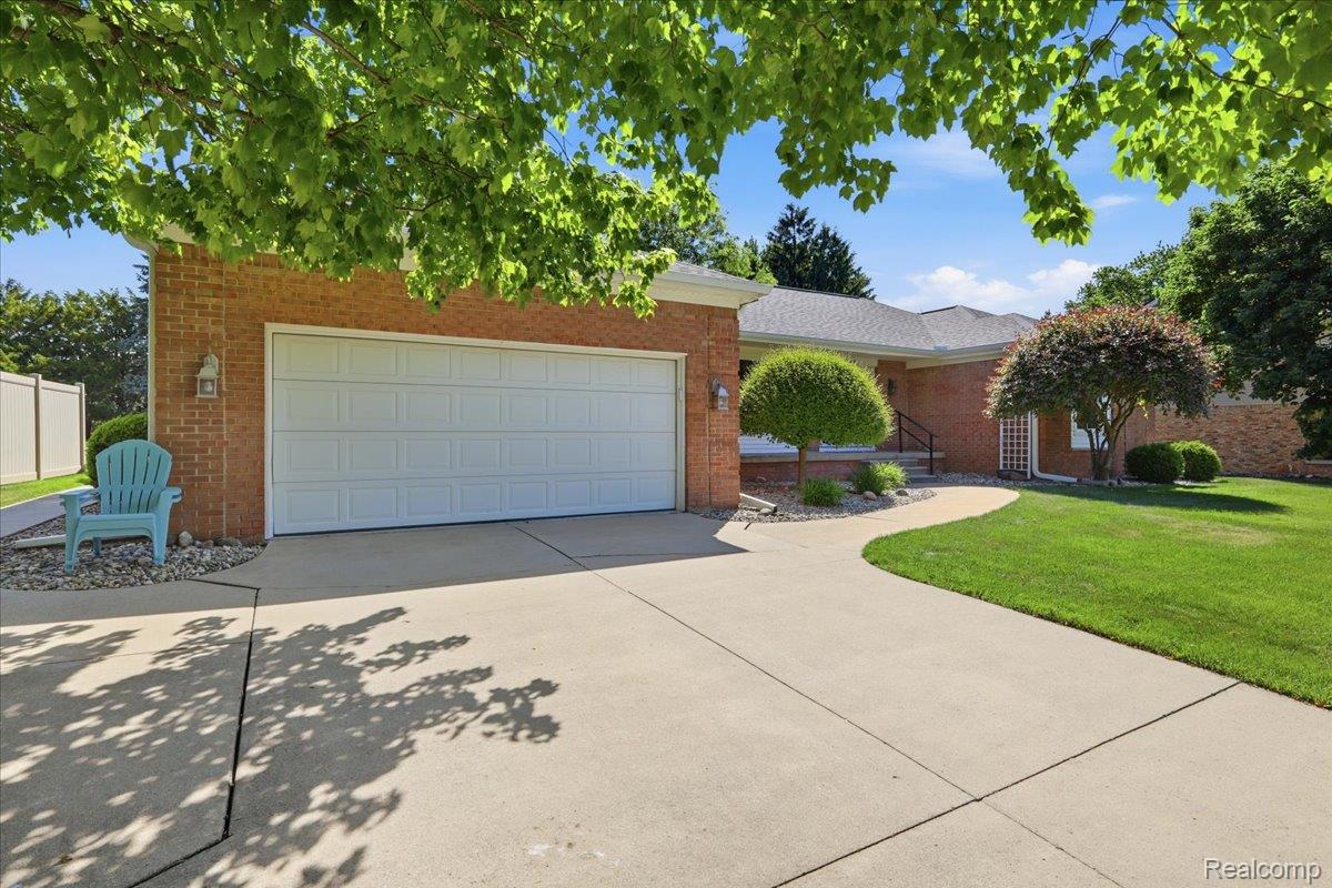 5048 Tree Hill Road Grand Blanc, MI 48439 - Photo 6 of 60 Brick exterior featuring a two-car garage with white panel doors, concrete driveway, front walkway, manicured lawn, and mature trees