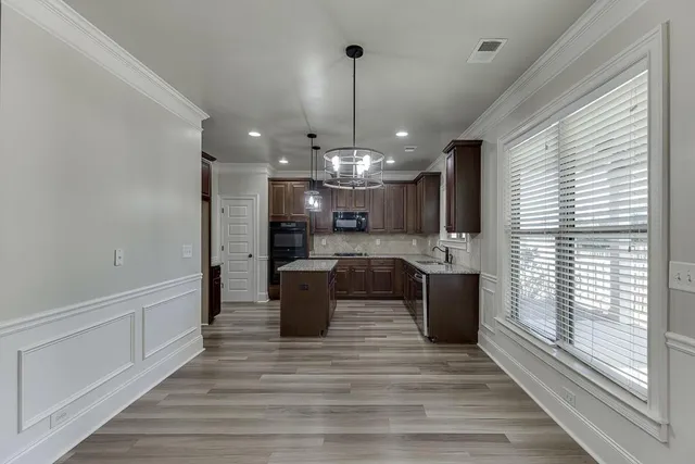 a kitchen with stainless steel appliances kitchen island granite countertop a refrigerator a sink dishwasher a stove and a dining table with wooden floor