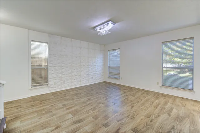 an empty room with wooden floor chandelier and windows