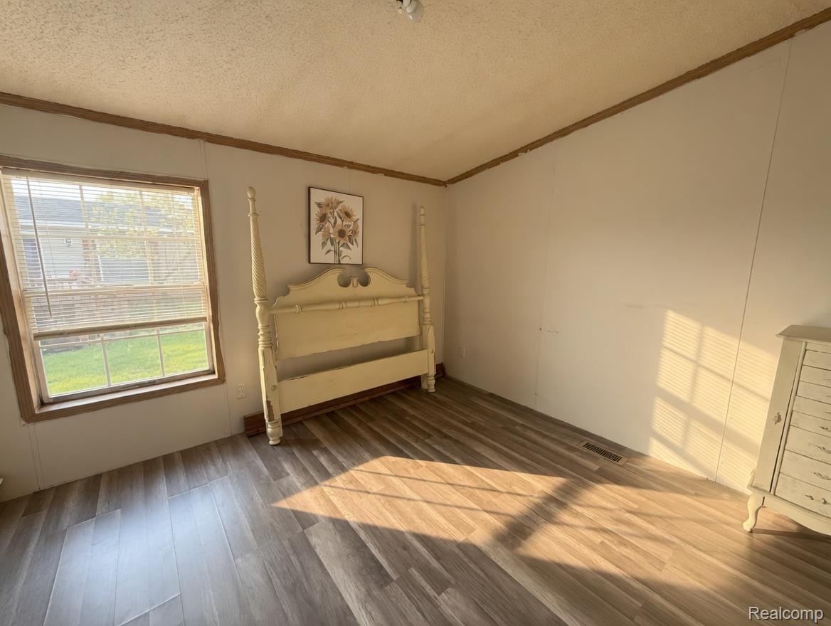 6988 McKean Road Ypsilanti, MI 48197 - Photo 20 of 31 Unfurnished bedroom featuring wood finished floors, a textured ceiling, and crown molding