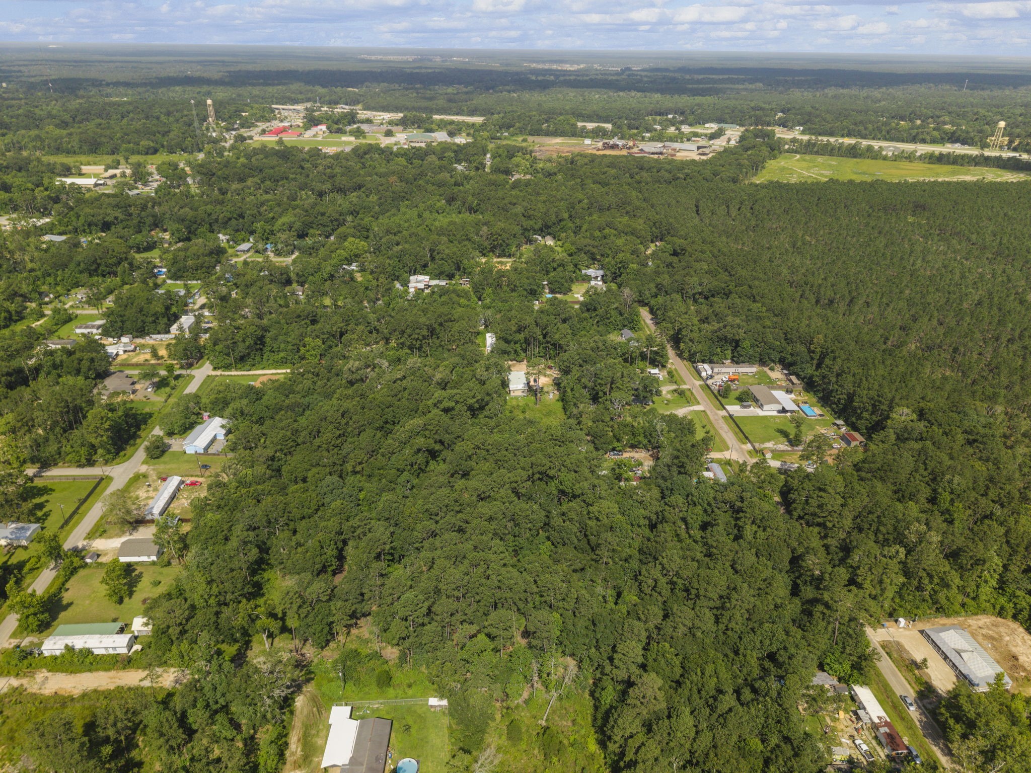 15597 Westgate Road Splendora, TX 77372 - Photo 5 of 14 Aerial Neighborhood View - Wide drone view captures the wooded Splendora setting, nearby residential pockets, and surrounding green landscape that frame the property area.