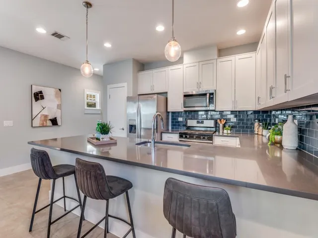 a kitchen with stainless steel appliances granite countertop a refrigerator a sink a stove a dining table and chairs with wooden floor