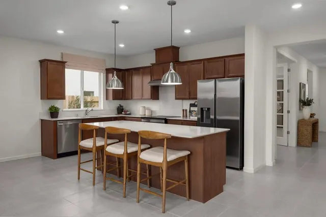 a kitchen with stainless steel appliances granite countertop a refrigerator a sink dishwasher a stove and a dining table with wooden floor