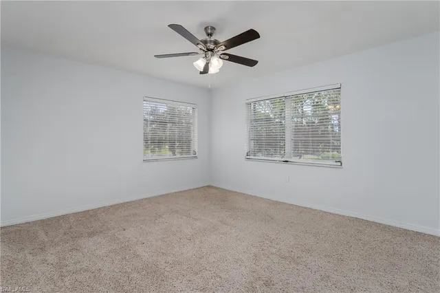 an empty room with ceiling fan and windows