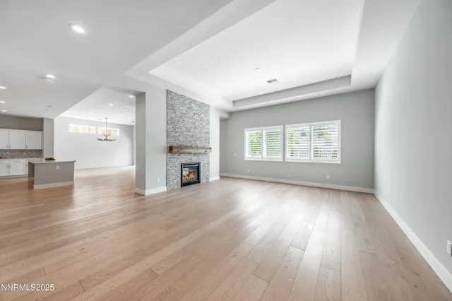 an empty room with wooden floor kitchen view and a fireplace
