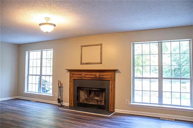 an empty room with wooden floor fireplace and windows