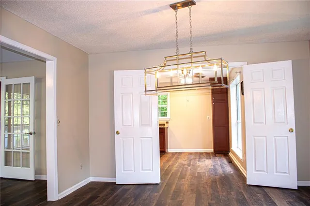 an empty room with wooden floor kitchen view and windows