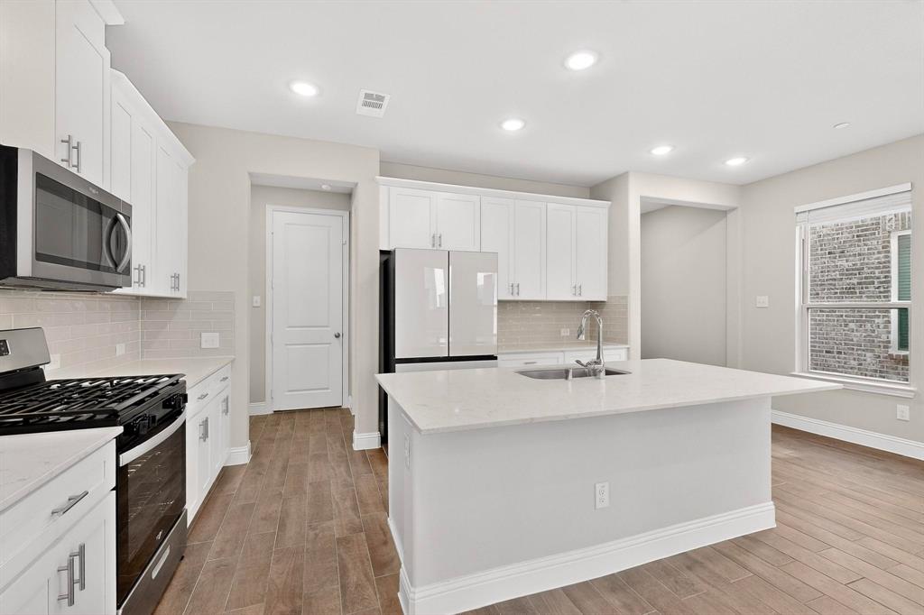 900 Heart Reef Road Plano, TX 75075 - Photo 13 of 40 a kitchen with kitchen island a stove a sink a refrigerator and cabinets