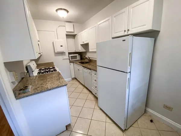 a kitchen with granite countertop a refrigerator a stove a sink and white cabinets