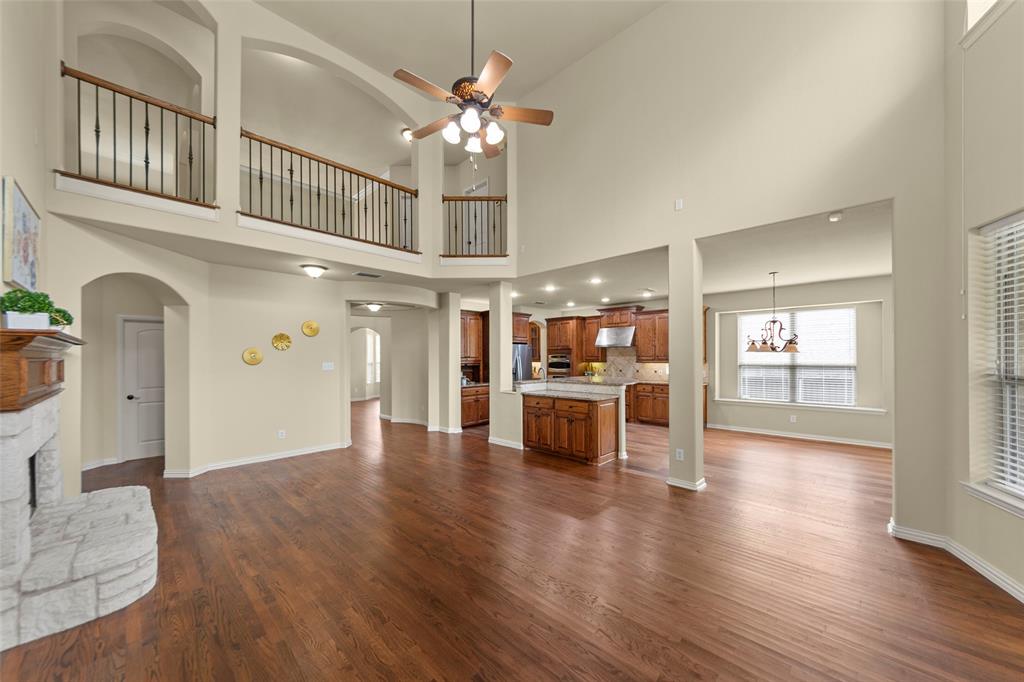 5143 Stream Crest Way Fairview, TX 75069 - Photo 10 of 35 Unfurnished living room with ceiling fan, dark wood-type flooring, arched walkways, a stone fireplace, and suspended lighting