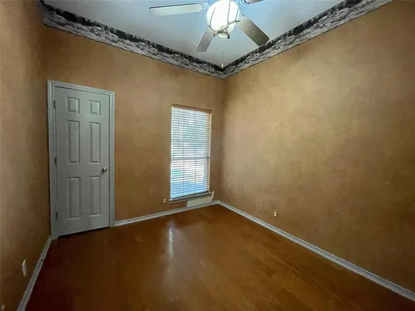 an empty room with a chandelier fan and wooden floor