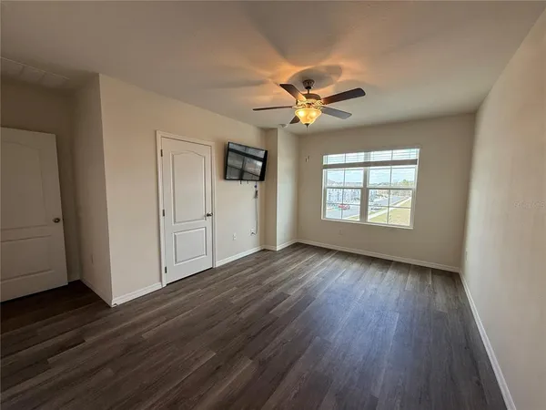 an empty room with wooden floor chandelier fan and windows