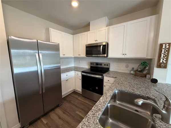 a kitchen with granite countertop a refrigerator a sink a stove a microwave and wooden cabinets