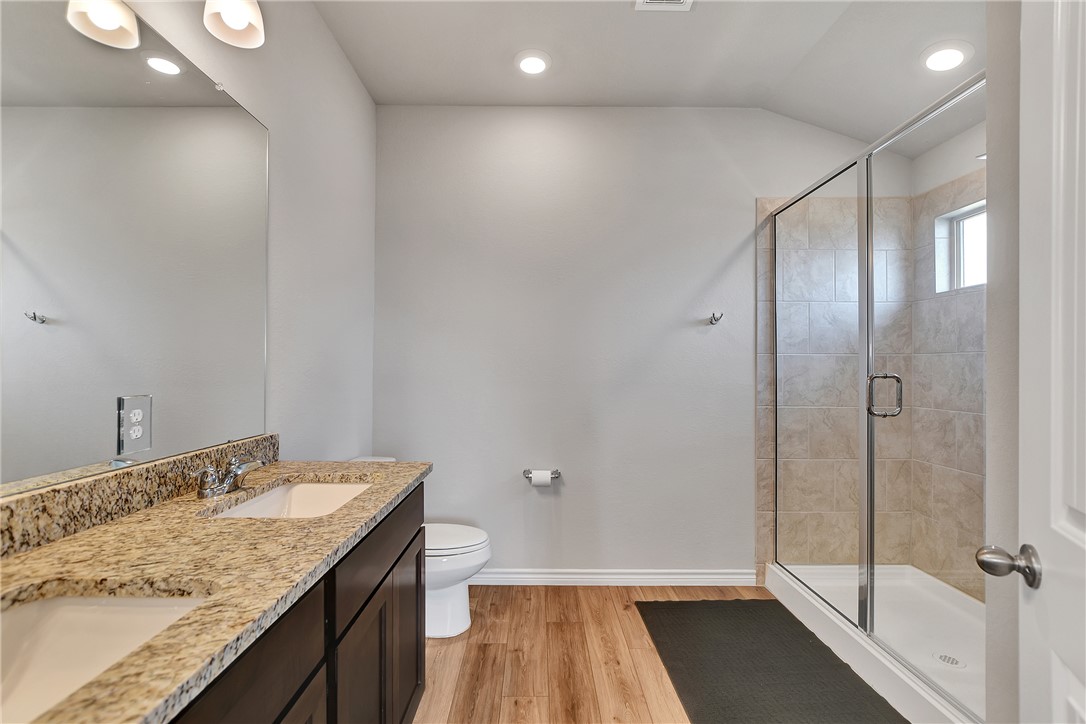 909 Davy Street Brenham, TX 77833 - Photo 19 of 35 Full bathroom featuring a shower stall, double vanity, light wood finished floors, recessed lighting, and vaulted ceiling