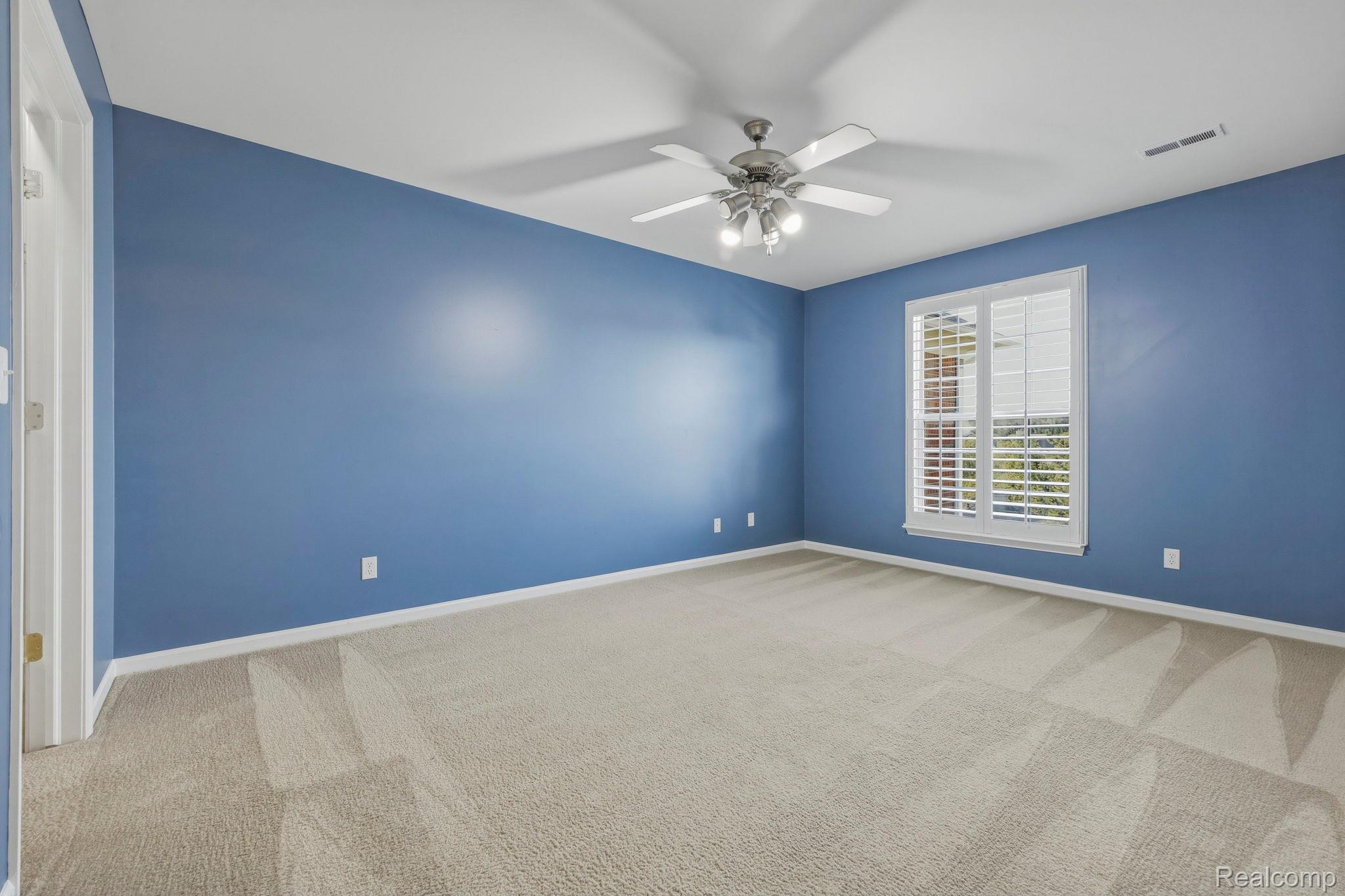 1905 Flagstone Circle Rochester, MI 48307 - Photo 23 of 33 Spacious room featuring broadloom carpet, a window with plantation shutters, a ceiling fan with integrated lighting, and blue painted walls