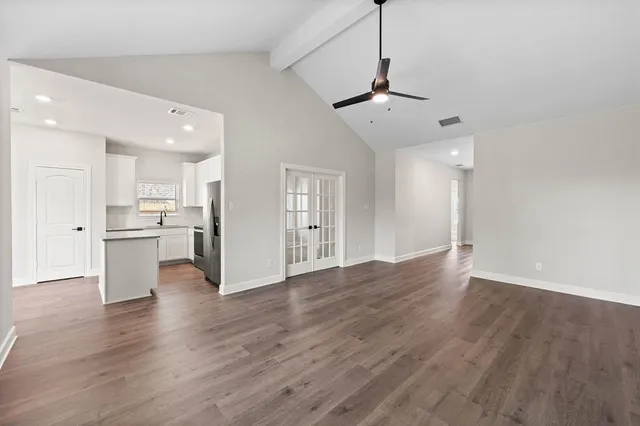 a view of an empty room with wooden floor and a kitchen