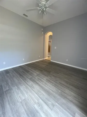 an empty room with wooden floor fan and windows