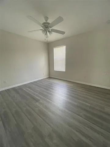 an empty room with wooden floor fan and windows