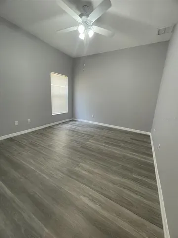 an empty room with wooden floor fan and windows