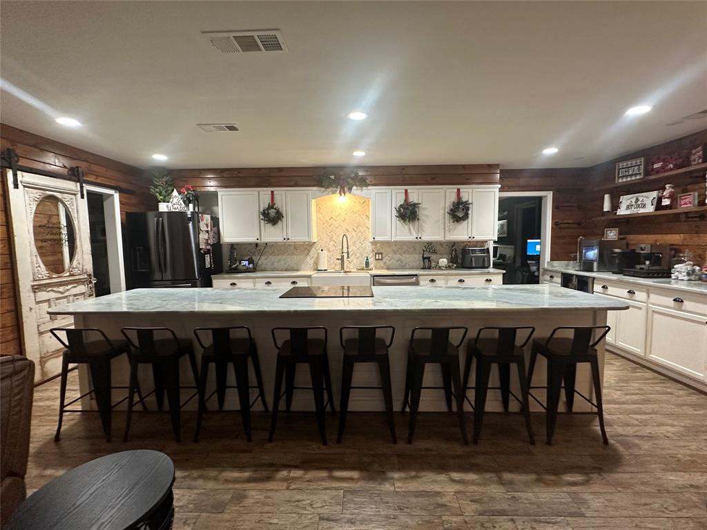 101 Twin Creek Road Comanche, TX 76442 - Photo 14 of 28 Kitchen with wooden walls, white cabinets, a spacious island, a barn door, and a kitchen breakfast bar