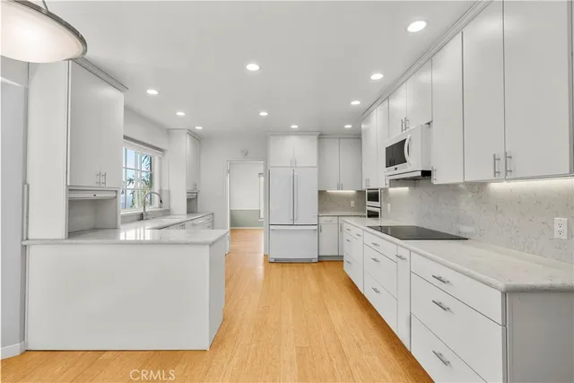 a open kitchen with stainless steel appliances granite countertop a refrigerator a sink dishwasher a stove and white cabinets with wooden floor