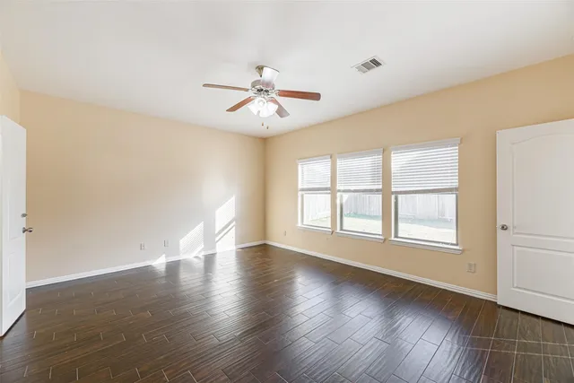 an empty room with wooden floor chandelier fan and windows