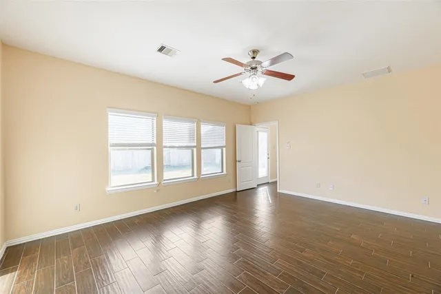 an empty room with wooden floor fan and windows