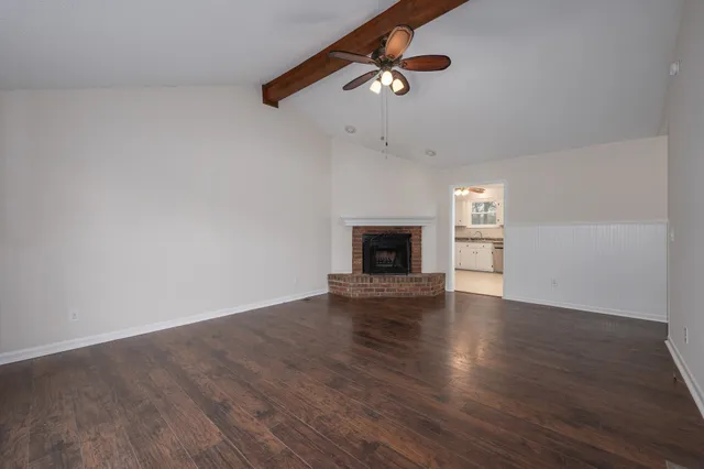 an empty room with wooden floor fireplace and windows