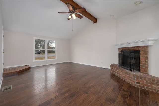 an empty room with wooden floor fireplace and windows