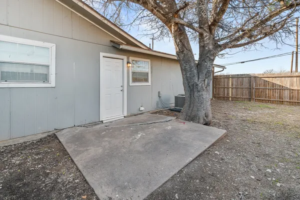 a backyard of a house with a large tree and wooden fence